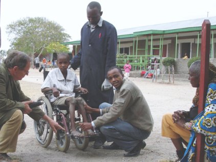 Colin, Moses and physioterapist Mokolo adjusting a small 6-wheeler for a disabled boy, his dad (seated) watcing and learning