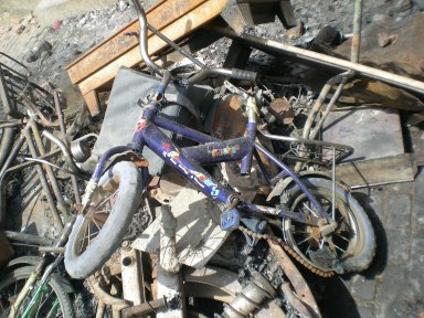 burnt child's bike on a heap of wasted things after the fires